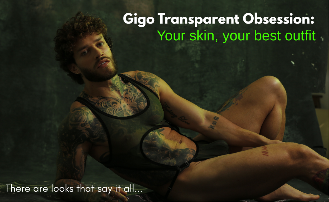 Tattooed model reclining in a dark sheer body with black trim and a circular opening at the abdomen.